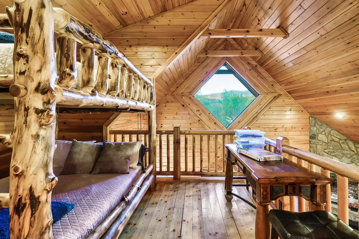 A cheerful interior space featuring a full-size bunk bed, a diamond-shaped window letting in natural light, and a small wooden desk. The scene suggests a family-friendly environment welcoming to children and guests.
