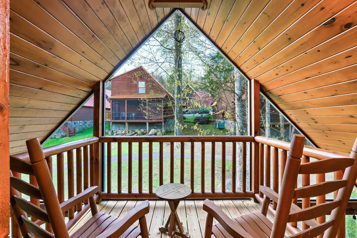 Rocking chairs line a wooden deck, bordered by a rustic railing with views of neighboring cabins in the distance. The inviting seating area is ideal for morning coffee or a restful pause after a hike, reinforcing the connection between the cabin and its scenic surroundings.