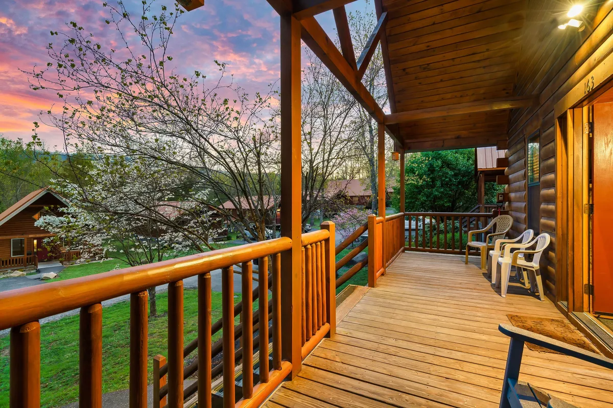 A warmly lit wooden porch at sunset, surrounded by trees and neighboring cabins in the background. Guests are shown relaxing on the porch, taking in the tranquil outdoor atmosphere and enjoying each other's company.