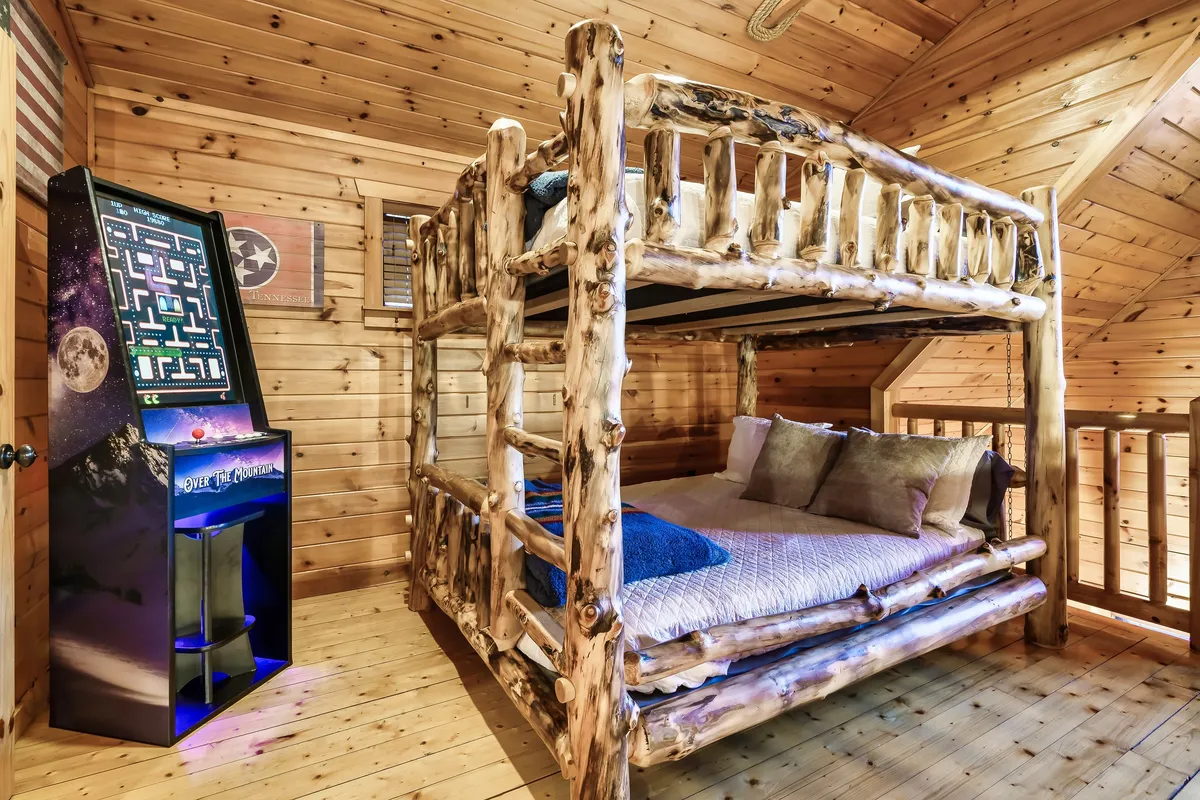 A playful corner featuring a bunk bed and a classic arcade game machine set against warm wooden walls. The nook is lively and inviting, perfect for families and groups looking to challenge each other and have fun together.